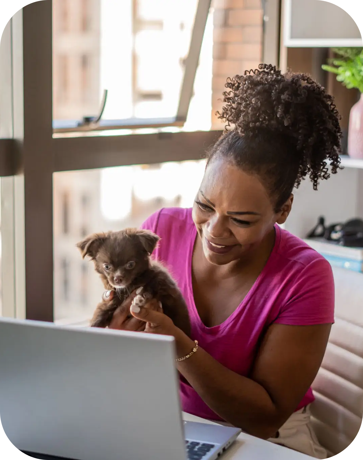 Woman smiling while holding a small dog near a laptop.