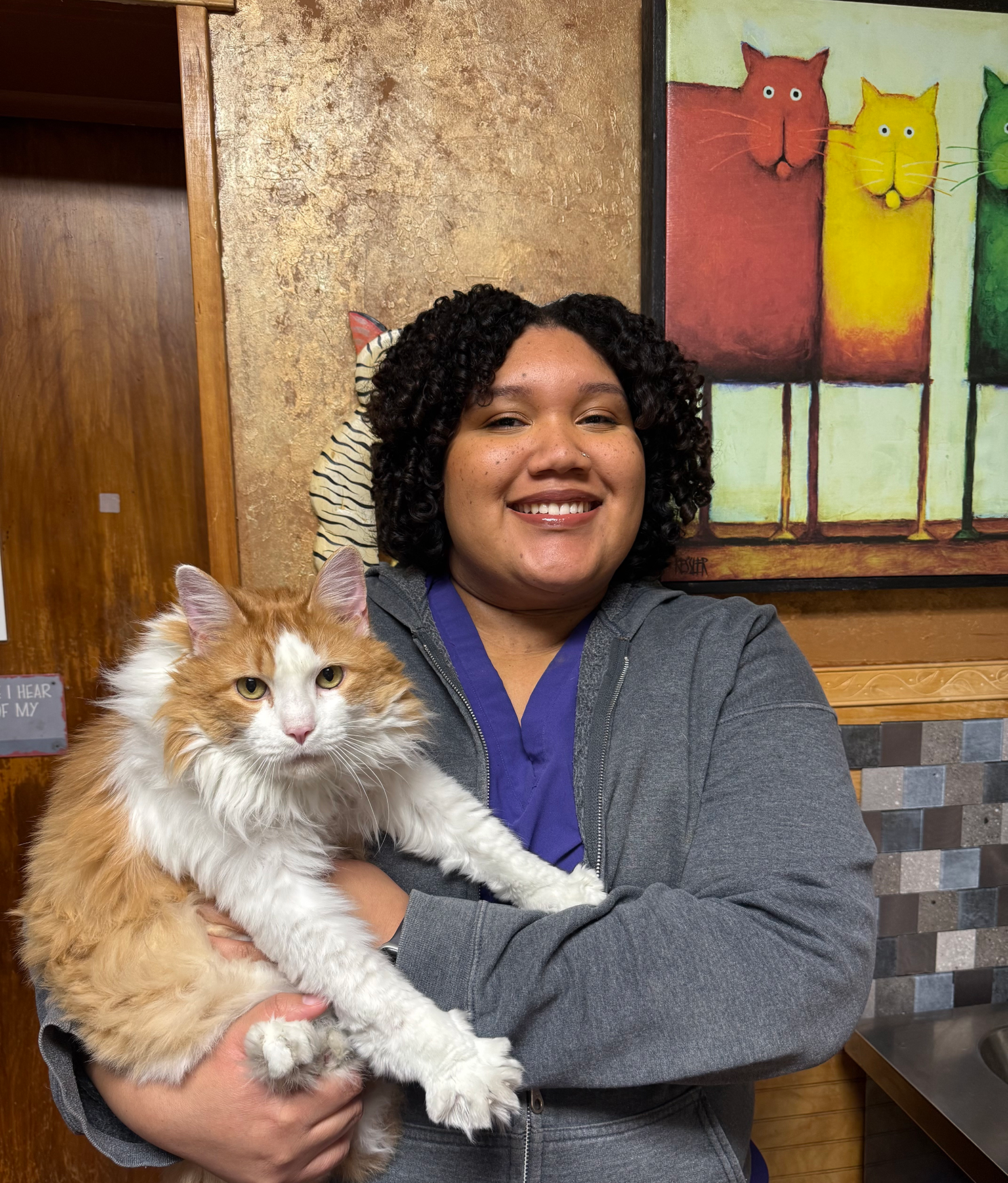 Person smiling and holding a fluffy orange and white cat indoors.